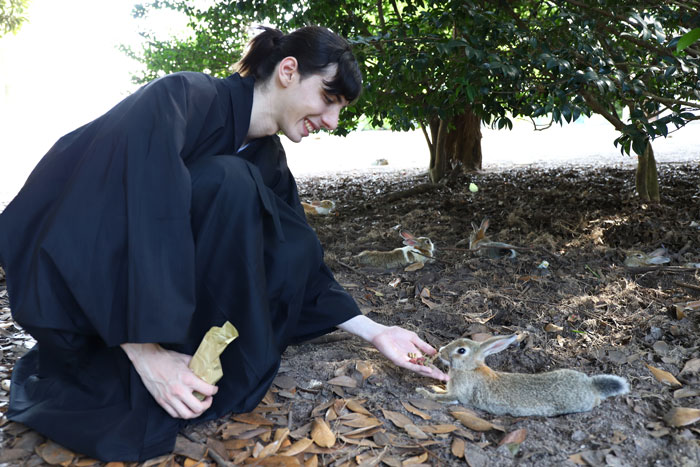 Man in hakama feeding a rabbit on Okunoshima (rabbit island) near Hiroshima, Japan